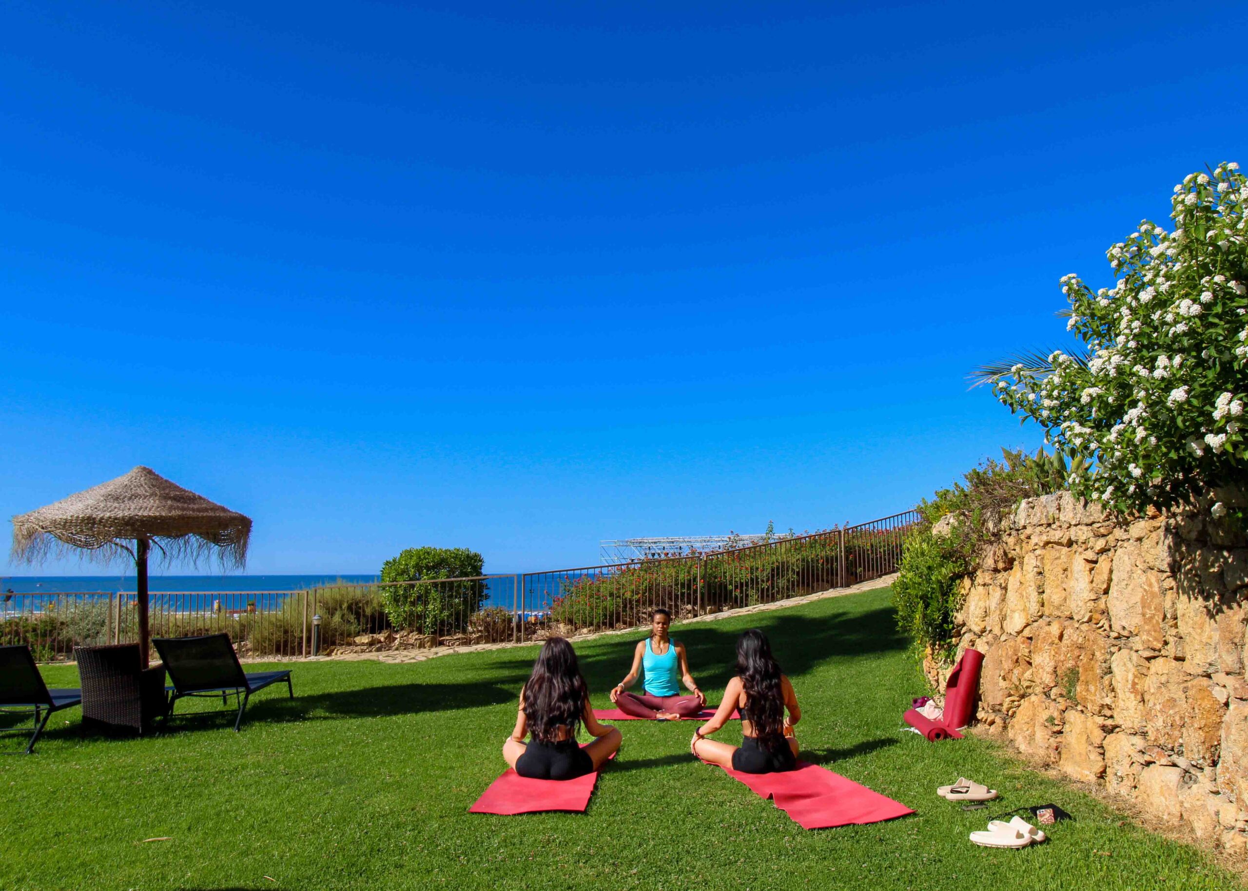 Três pessoas sentadas a fazer uma aula de yoga no jardim do hotel AP Oriental Beach