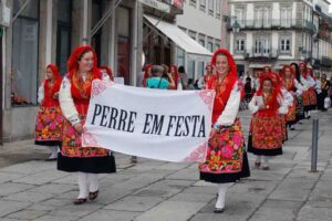 Raparigas com trajes tradicionais de Viana do Castelo a carregar um cartaz que diz "Perre em Festa"